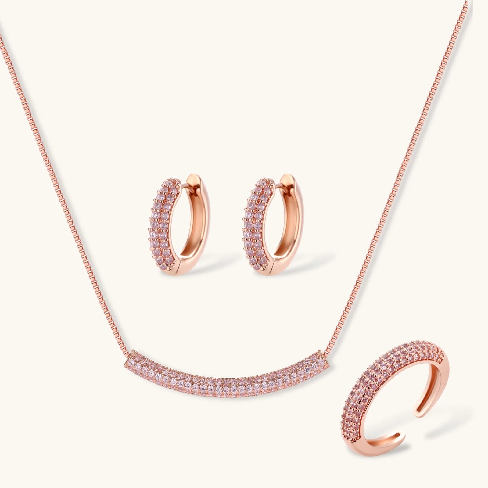 Rose gold jewelry set with pavé cubic zirconia stones including curved necklace, hoop earrings, and adjustable ring on cream background.