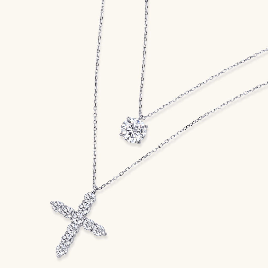 Two delicate sterling silver necklaces with moissanite stones - one solitaire pendant and one cross pendant on white background.