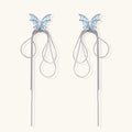 Long silver-tone earrings with powder blue enamel butterfly studs and flowing chain tassels on cream background