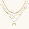 Four-layer gold necklace with herringbone chain, disc charms, and crescent moon pendant on cream background