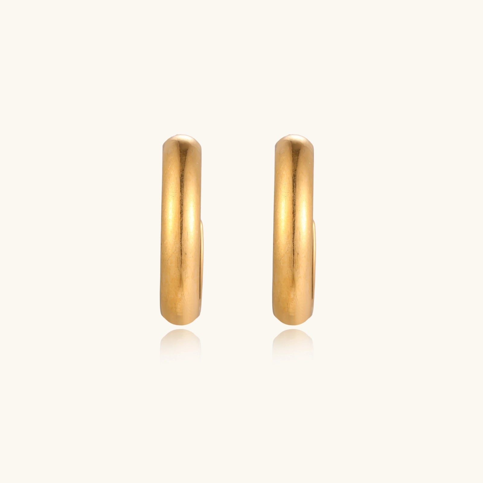 Chunky tubular hoop earrings in warm 14K gold-plated finish with smooth polished surface on cream background.