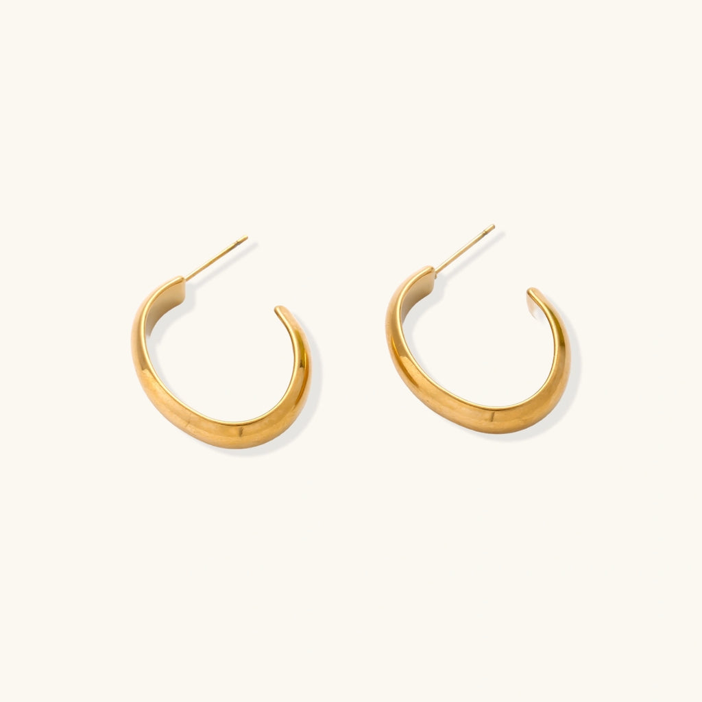 Chunky tubular hoop earrings in warm 14K gold-plated finish with smooth polished surface on cream background.