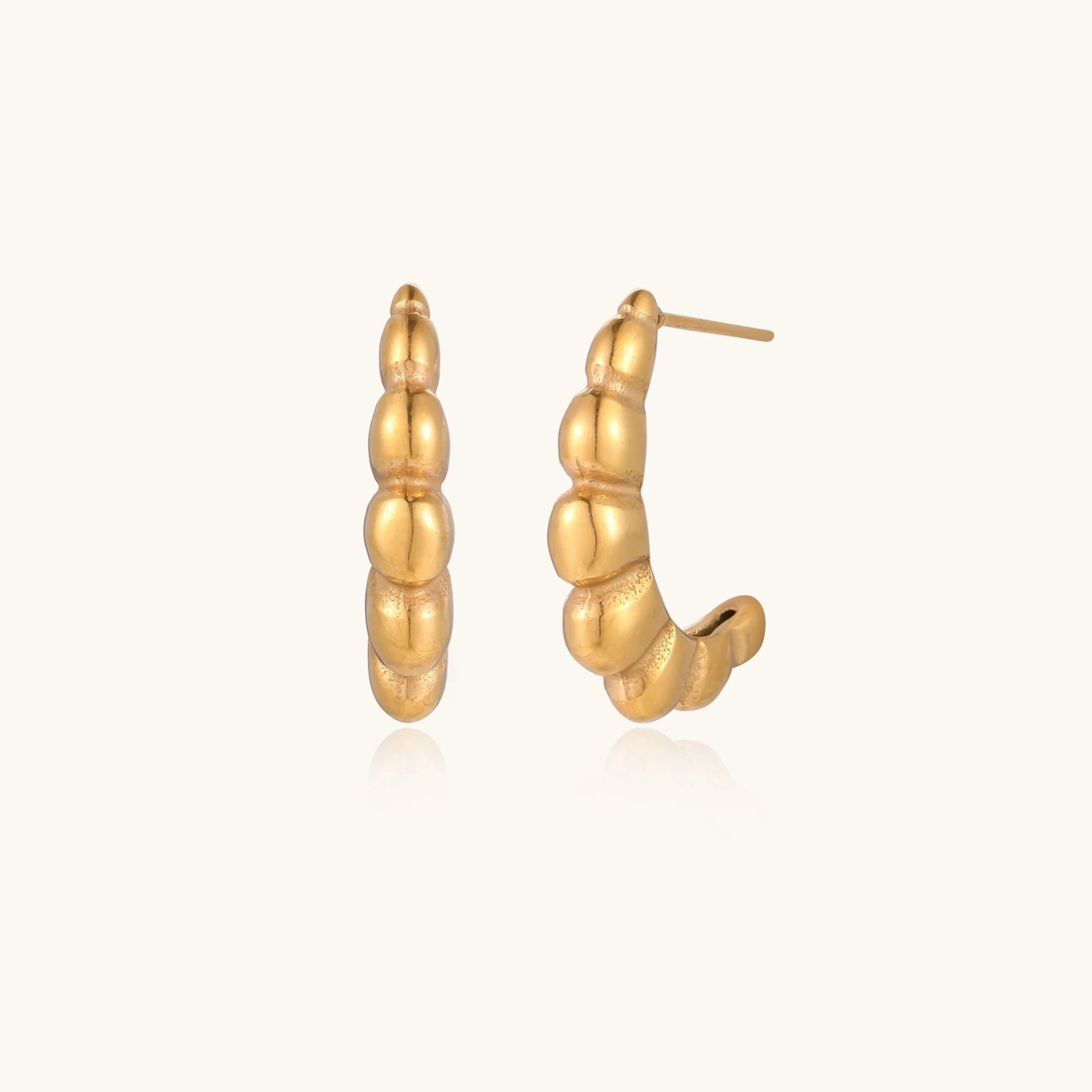Gold-plated chunky hoop earrings with ridged bubble texture on cream background