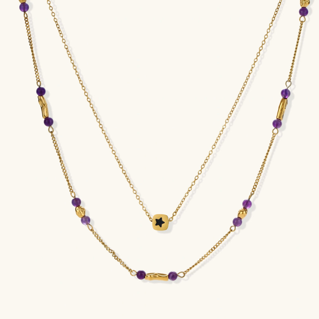 Two layered gold-tone necklaces with purple stone beads and star pendant against cream background.