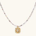 Ornate gold-plated pendant necklace with multicolored gemstone beads in purple, pink and clear tones on white background